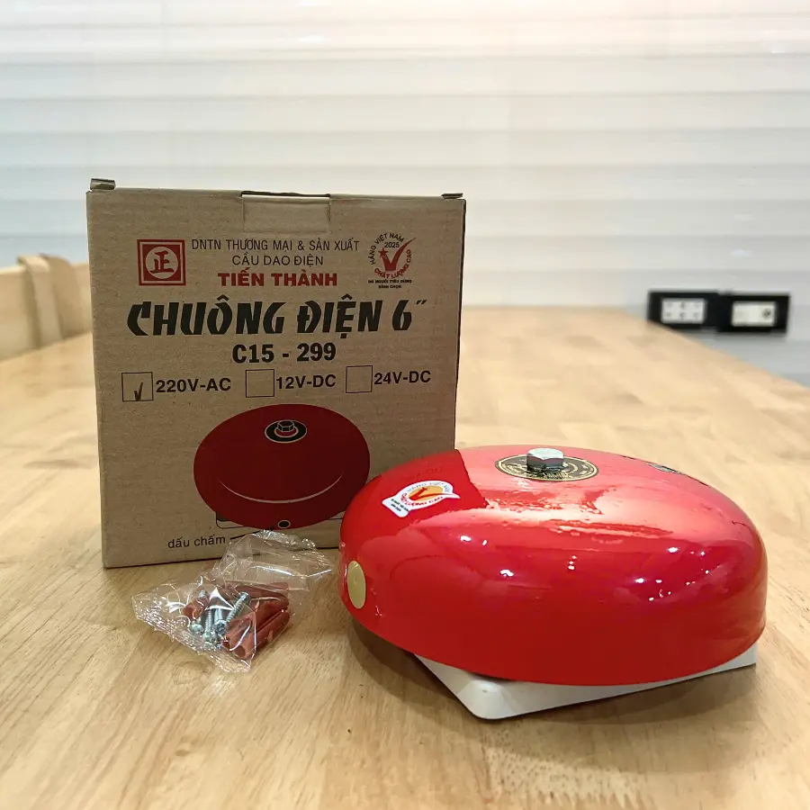 Chuông điện 6 inch màu đỏ đặt cạnh hộp Tiến Thành C15-299 và túi phụ kiện lắp đặt trên bàn gỗ