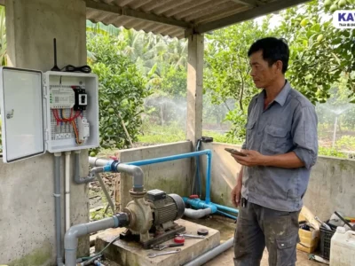 Người đàn ông sử dụng điện thoại cạnh máy bơm và tủ điều khiển 4G tại nhà vườn